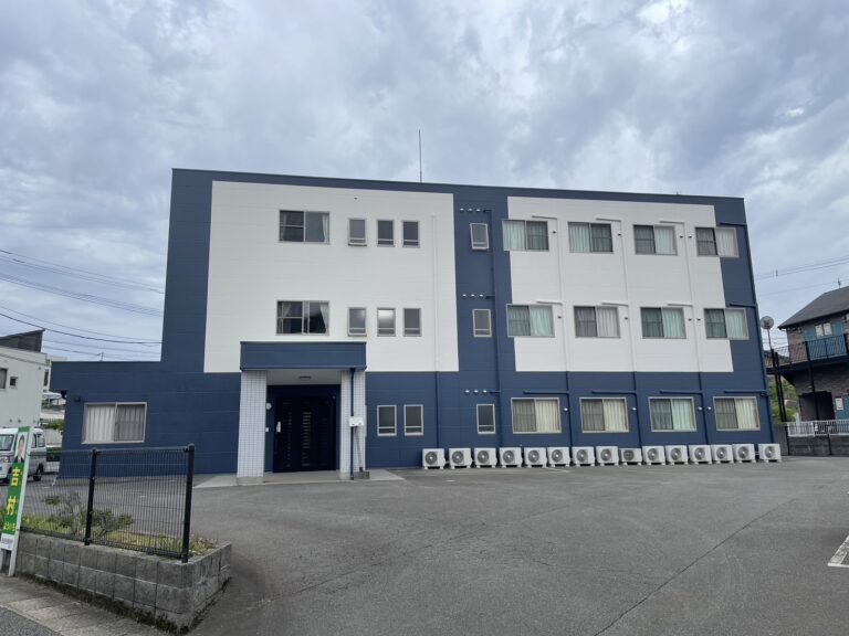 紺と白を基調とした介護施設の3階建て建物外観。駐車スペース完備。